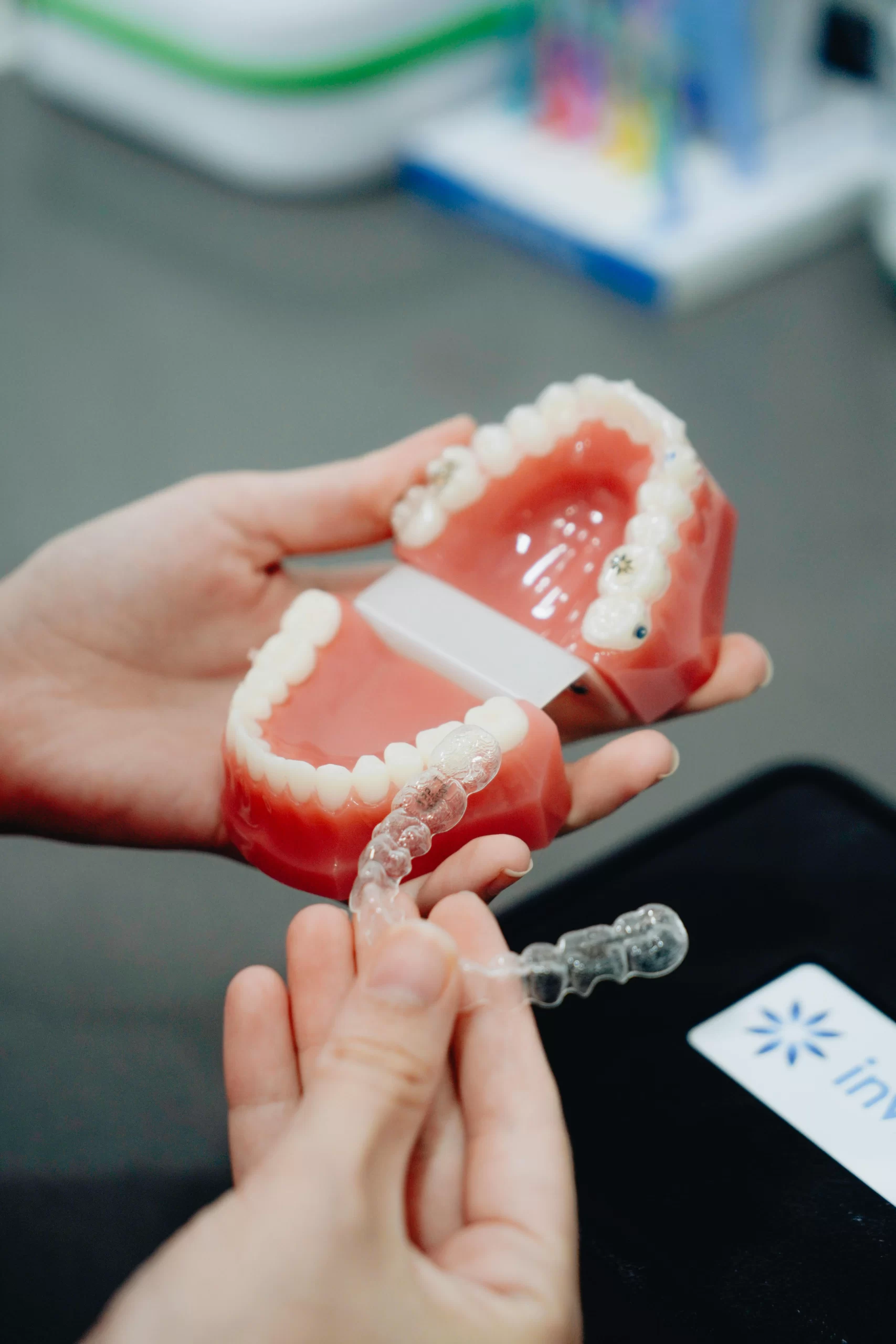 Person holding a dental model and an Invisalign clear aligner, demonstrating how the aligner fits over the teeth.